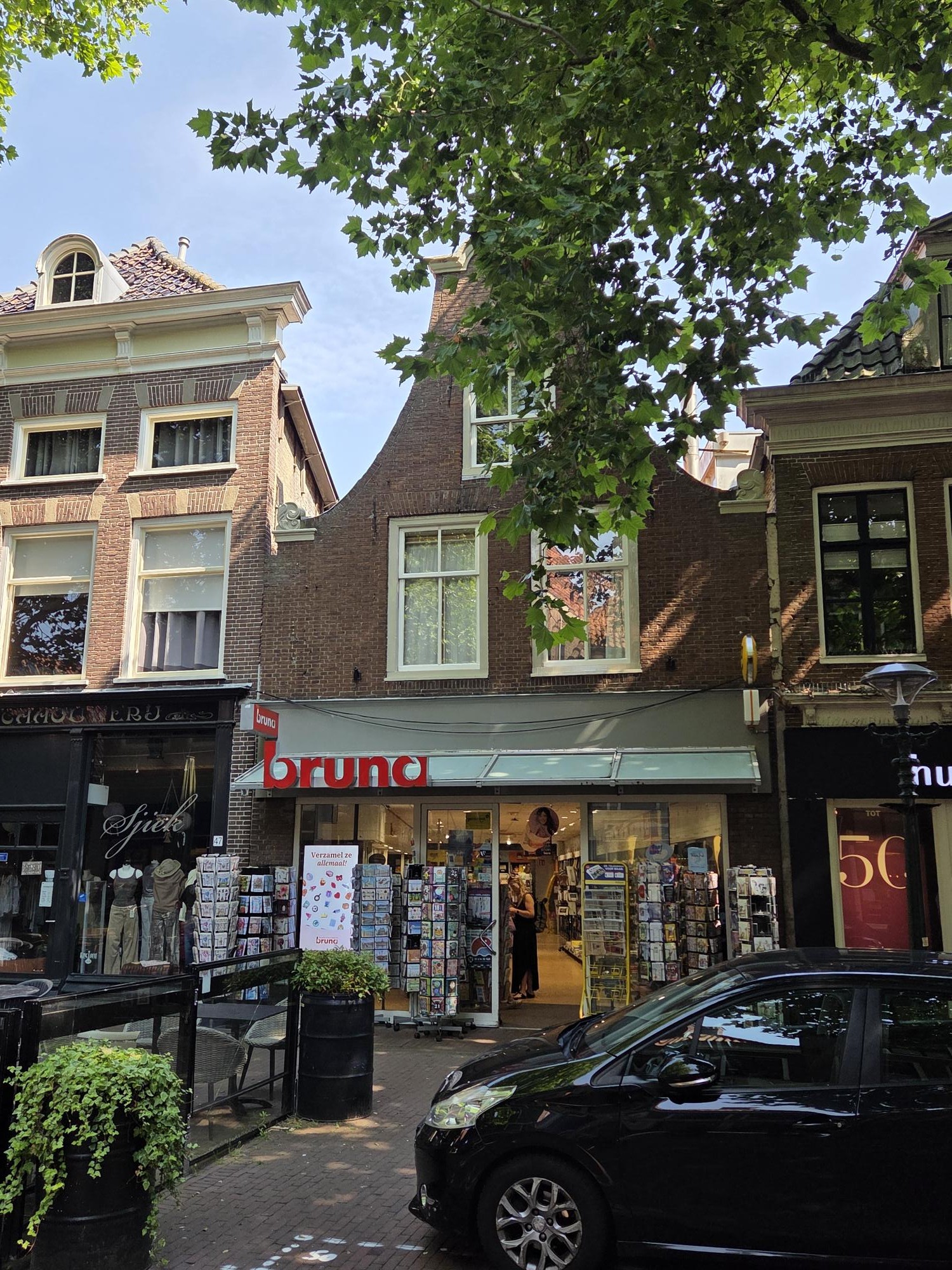 Vooraanzicht van de Bruna-winkel in een historisch bakstenen pand met een zwarte auto op de voorgrond.