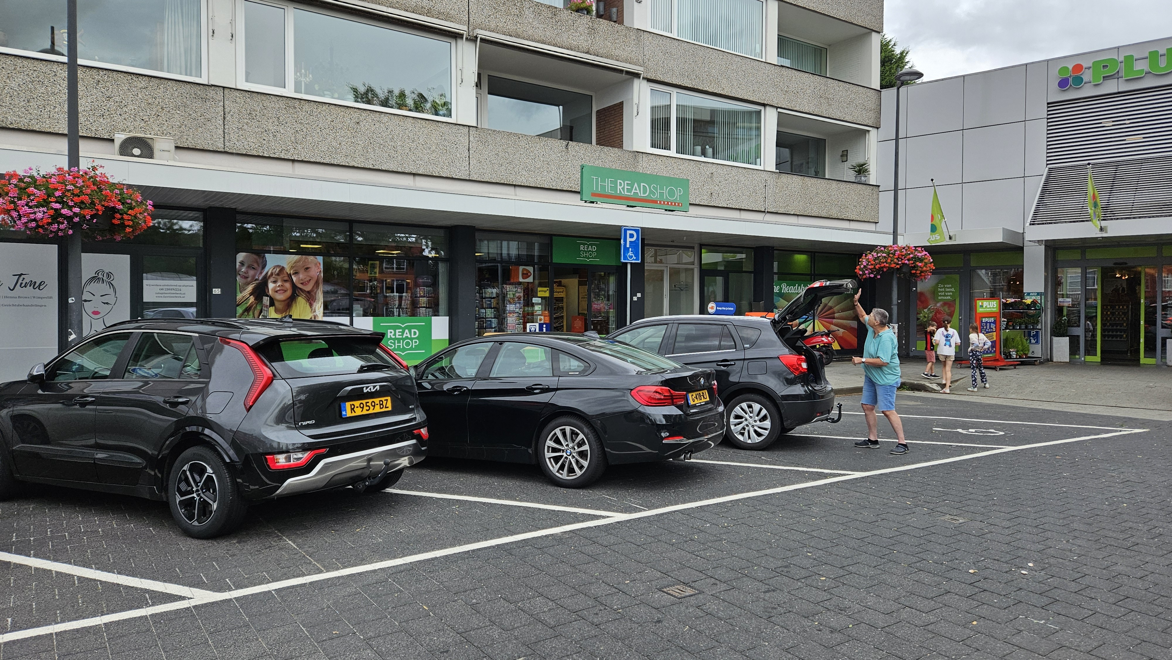 Parkeerplaats met drie zwarte auto's voor de gevel van The Read Shop Express en een nabijgelegen PLUS supermarkt.
