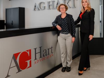 Twee personen staan naast een balie met logo van AG Hart Advocaten in een modern kantoorinterieur.