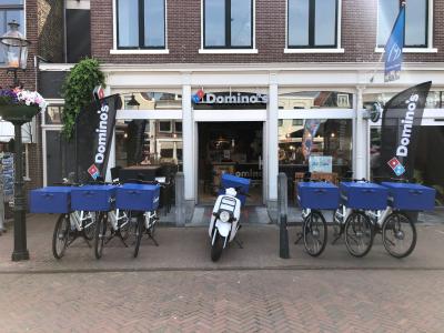 Rij met fietsen en scooter voor een Domino's shop, klaar voor bezorging.