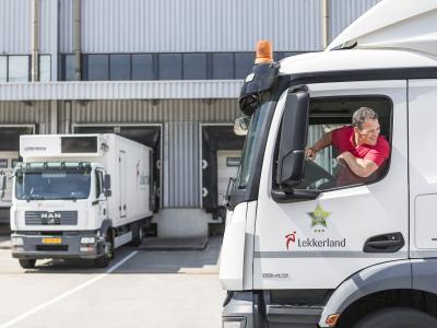 Vrachtwagens van Lekkerland bij een laadperron waarbij een chauffeur uit zijn cabine kijkt.