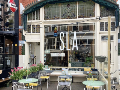 Vooraanzicht van een SLA-restaurant met terrasstoelen en tafels op een zonnige dag.