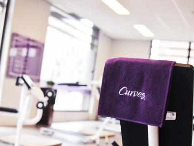 Binnenruimte van een Curves-fitnessstudio met paarse handdoek op een fitnessapparaat.