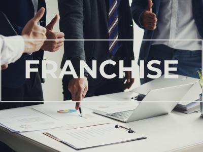Zakelijke bespreking met grafieken en laptop, focus op de term Franchise, handen wijzen en duimen omhoog.