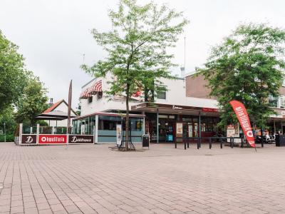 Exterieur van Kwalitaria Délifrance De Beuk met terras en opvallende rode vlag op een zonnige dag.