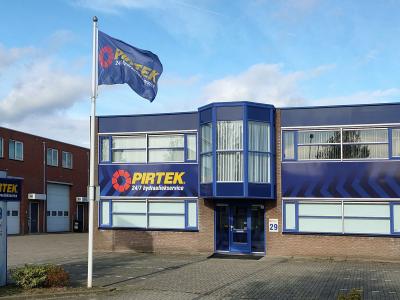 Pand van Pirtek met bedrijfslogo's en vlaggen op een industrieterrein in de Benelux.