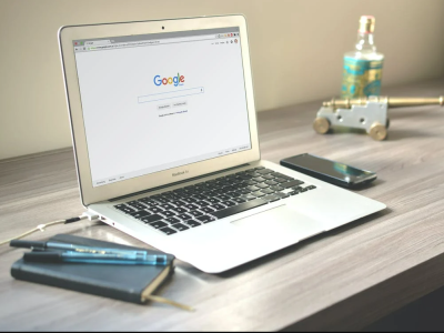 Een opengeklapte laptop op een bureau met Google op het scherm, naast een notitieboek en een smartphone.