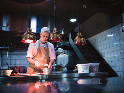 Een kok bereidt een gerecht in een professionele keuken onder warme hanglampen.