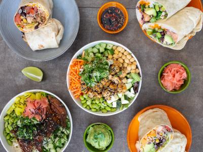 Diverse gerechten van de fusionkeuken met wraps en kleurrijke poké bowls, gepresenteerd met verschillende sauzen.