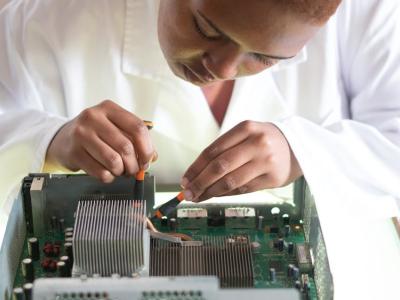 Technicus in witte werkkleding werkt geconcentreerd aan het repareren van elektronica met behulp van gereedschap.