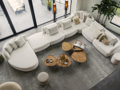Luxe woonkamer met grote loungebank, houten bijzettafels, poefs, en veel kussens in een modern ingericht interieur.