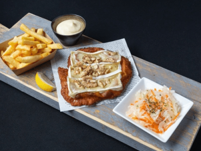 Schnitzel met brie en noten, geserveerd met friet, mayonaise en een salade van witte en oranje groente op een houten plank.