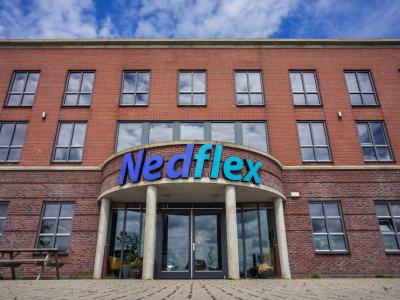 Vooraanzicht van het Nedflex kantoorgebouw met het logo boven de entree en een zonnige lucht op de achtergrond.