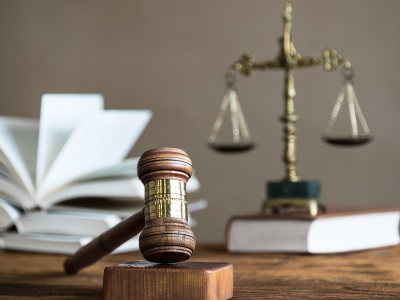 Houten hamer op een tafel met op de achtergrond een opengeslagen boek en een weegschaal van justitie.