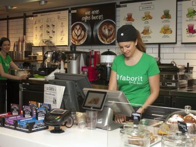 Medewerkers in een koffiebar nemen bestellingen op achter de toonbank, met diverse dranken en snacks uitgestald.
