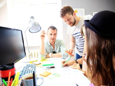 Team van vier mensen bespreekt en werkt samen aan een project aan een bureau met documenten en kantoorbenodigdheden.