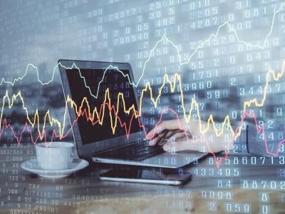 Laptop met handen op toetsenbord en meerdere financiële grafieken en cijfers overlappen elkaar op transparante achtergrond.