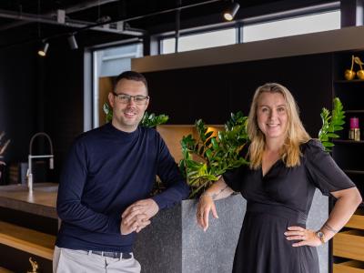 Twee personen poseren in een moderne showroom van Marquardt Küchen, omgeven door stijlvolle keukeninterieurs.