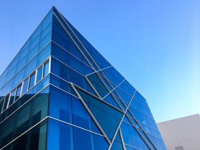 Modern kantoorpand met blauwe glazen gevels tegen een heldere lucht.
