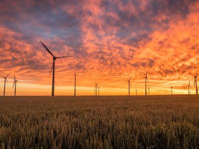 Windturbines op een veld bij zonsondergang, met een kleurrijke oranje lucht op de achtergrond.