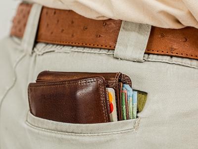 Bruine leren portemonnee vol met pasjes en geld steekt uit de achterzak van een crèmekleurige broek.