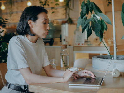 Ondernemer werkt geconcentreerd op laptop in een modern café, omringd door planten en een koffiekop op tafel.