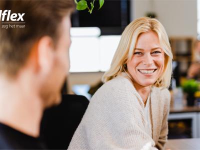 Vrouw glimlacht tijdens een gesprek in een modern kantoor met het Nedflex-logo linksboven.