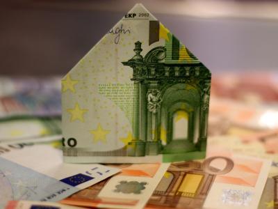 Een model van een huis gevouwen uit een eurobiljet, met andere eurobiljetten eromheen verspreid.
