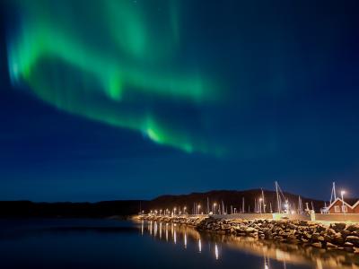 Noorderlicht boven een verlichte haven met huisjes en boten aan een rustige kustlijn in Noorwegen.