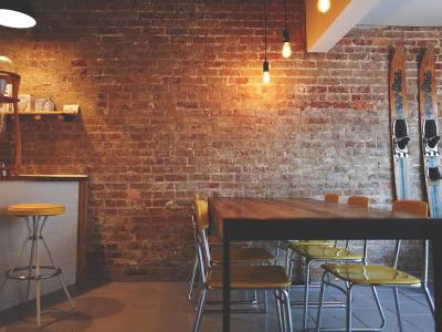 Industrieel ingerichte restaurantinterieur met bakstenen muur, houten tafel, gele stoelen en hangende lampen.