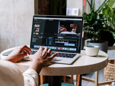 Persoon werkt op een laptop aan een videoproject in een moderne kantooromgeving met veel groen.