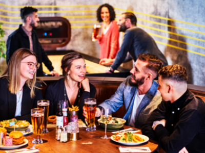 Groep mensen geniet van eten en drinken in een sfeervolle omgeving bij een tafel met diverse gerechten en drankjes.
