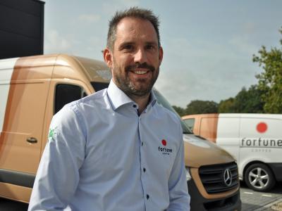 Man in verzorgd uniform staat voor bestelwagens van Fortune Coffee.