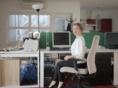 Zakelijke vrouw aan een bureau met computer, zittend en glimlachend in een moderne kantooromgeving.