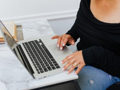 Persoon werkt op een laptop aan een bureau met een open boek ernaast.