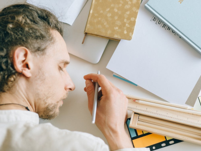 Een vermoeide persoon rust hoofd op bureau naast notitieboek met woord burn-out.