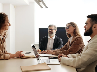 Vier personen in een zakelijke bespreking aan een tafel met laptops en notitieblokken.