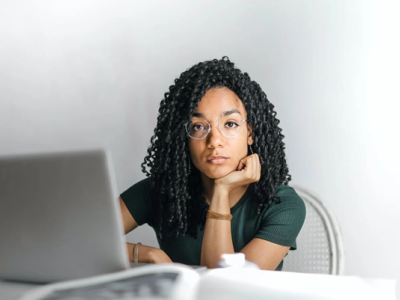 Vrouw met bril denkt na terwijl ze achter een laptop zit in een lichte, moderne omgeving.