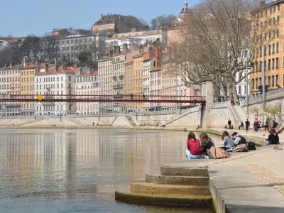 Gezellige sfeer langs de rivier in Lyon met kleurenrijke gebouwen, wandelaars en mensen zittend aan het water.