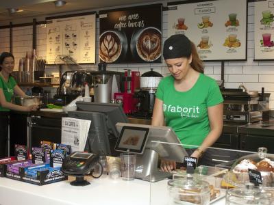 Medewerkers van een koffieketen bedienen klanten achter de toonbank met diverse producten en apparatuur.