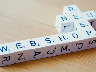Witte houten blokken vormen de woorden webshop, structuur en optimaal op een houten tafelblad.