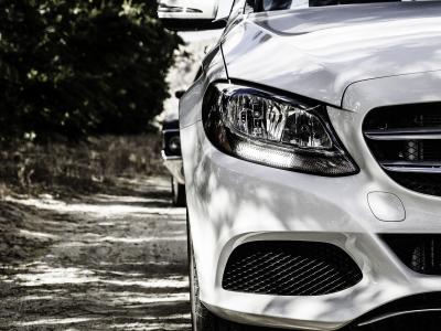 Voorkant van een luxe witte auto geparkeerd op een zandweg met schaduwen van bomen op de achtergrond.