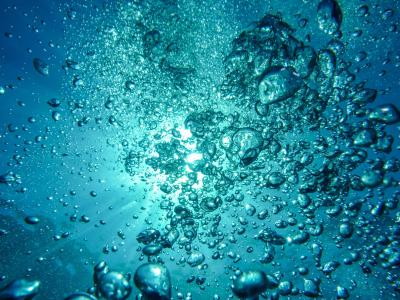 Opstijgende waterbellen in helder blauw water met zonlicht dat door het oppervlak schijnt.