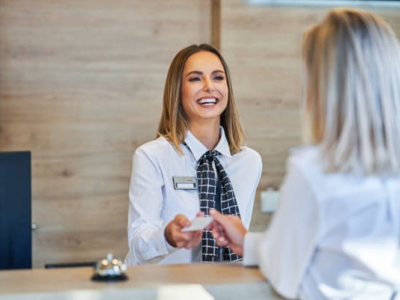 Receptioniste in professionele bedrijfskleding overhandigt een kaart aan een klant bij de balie.