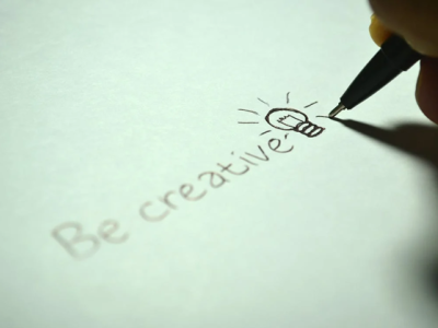 Hand schrijft Be creative met een tekening van een gloeilamp als inspiratie op wit papier.