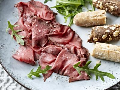 Plak met dungesneden rosbief, rucola en rustiek brood op een lichtblauwe schaal.