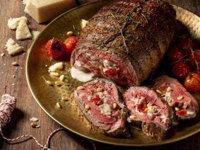 Gesneden rollade gevuld met kaas en tomaten, gereserveerd met pijnboompitten en Parmezaanse kaas op een houten tafel.