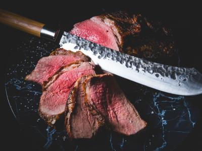 Grote mes naast dungesneden rosbief op donker marmeren oppervlak.