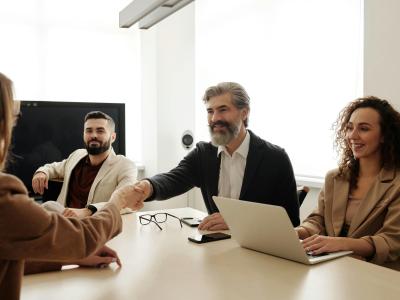 Vier mensen in een moderne vergaderruimte, twee personen schudden elkaar de hand over een tafel.
