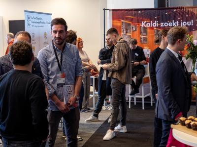 Mensen netwerken en bespreken franchiseconcepten op de Franchise+ Beurs in een levendige beursomgeving.